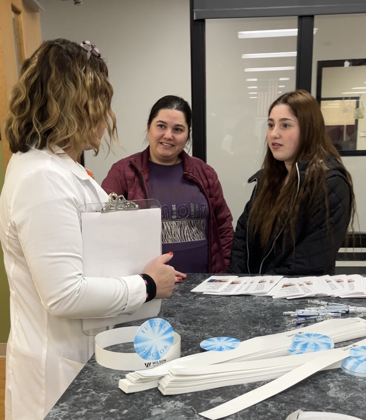 Health teacher speaking with two guests at an event.